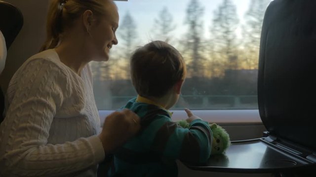 Mother and son with toy in the train at sunset. They looking out the window, mom showing something to kid and talking to him