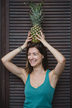 Cute laughing girl holds a pineapple on head