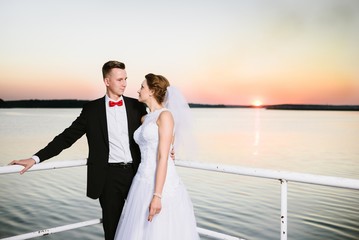 Naklejka premium Bride and groom on the pier at sunset.