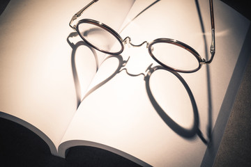 still life photography : eyeglasses on blank page of opening book with heart shape shadow in...