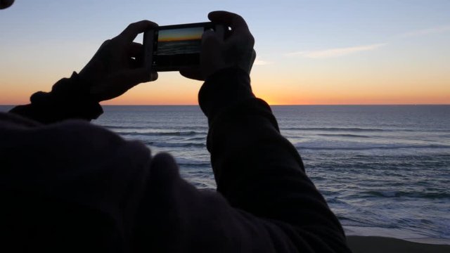 Man taking cell phone photo at sunset