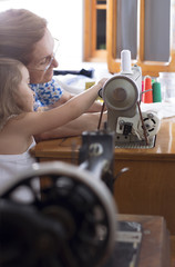 Little granddaughter helping her grandmother to sew. Different generations spending time together