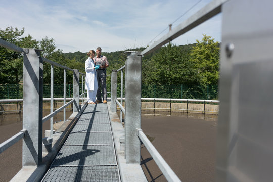 Worker and lab technician taking sample from tank in water purification plant