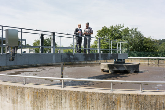 Worker and manager standing on metal bridge over sedimentation tank in sewage treatment pant