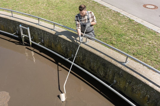 Worker taking water sample out of clarifier tank of sewage treatment plant