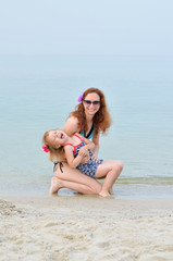 Young woman with a child on the sandy shore, summer vacation.