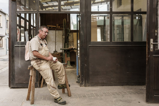 Craftsman having cup of sitting on wooden stairs in carpentry wo