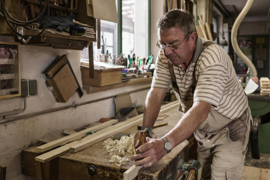 Craftsman in carpentry workshop smoothing wooden workpiece with planer