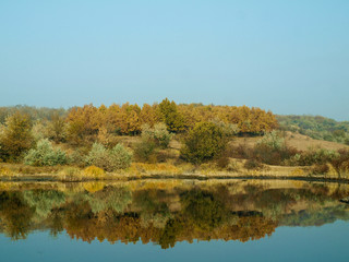 Красивый осенний пейзаж на берегу отражается в спокойной глади реки погожим днем 