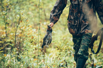 Male hunter in the autumn forest. A man holding a gun. Hunter holding a bird grouse.