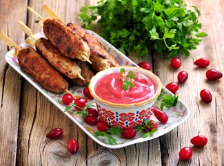 Homemade sauce dogberry with meat kebabs on wooden skewers.