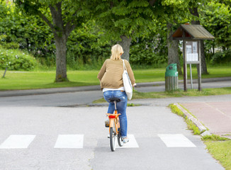 An unidentified woman is riding a bike on the road.
