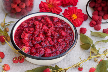 Raspberry jam in a bowl with fresh raspberry and flowers, rustic style.