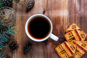 A cup of tea and cookies on a wooden table. Near the Christmas tree branch, pine cones and...