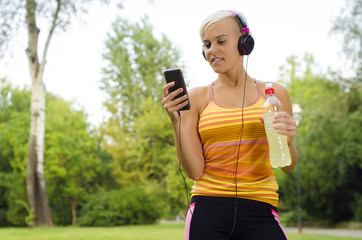 Young athletic woman with smart phone, headphones and refreshing drink