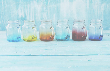 colored glass jars with handles on a wooden blue background