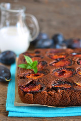 Chocolate cake with plums on a dark background with milk 