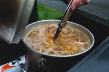 A concept of cooking field red colored meat soup on a bonfire or portable gas stove on camping in Norway