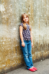 Outdoor vertical portrait of a cute little 7 year old girl wearing bright red shoes and denim jeans