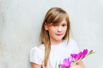 Fototapeta premium Close up portrait of a cute little 7 year old girl with purple flower