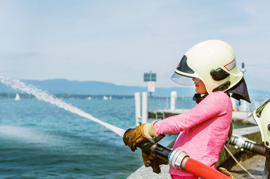 Little girl pretending to be firefighter, open doors day at fire station. Future profession for children. Educational programme for schoolkids