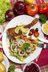 Fried scorpaena scrofa with salad on the plate and serving at the table with fresh vegetables.