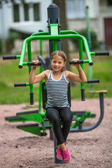 Fototapeta na wymiar Little girl is engaged in sport fitness equipment outdoor.