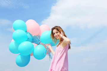 Beautiful young woman with colorful balloons against blue sky