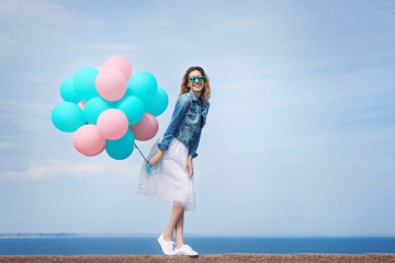 Beautiful young woman with colorful balloons on sea front