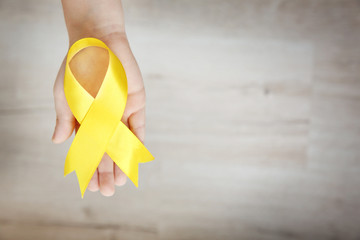 Baby hand holding yellow ribbon on color background