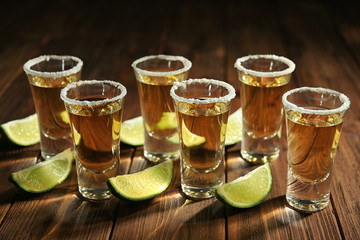 Gold tequila shots in a row with lime slices and salt on wooden background