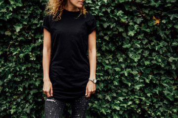 Cropped image of young hipster girl with curly hair wearing a blank black t-shirt and black jeans....
