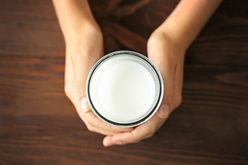 Fototapeta na wymiar Female hands holding glass of fresh milk on wooden background