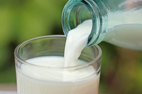 Milk pouring from a bottle into a glass, outdoors