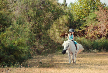 Little girl on the horse. White poni.