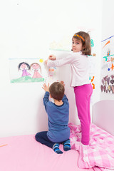 Cute little children setting their drawings on the wall of their room