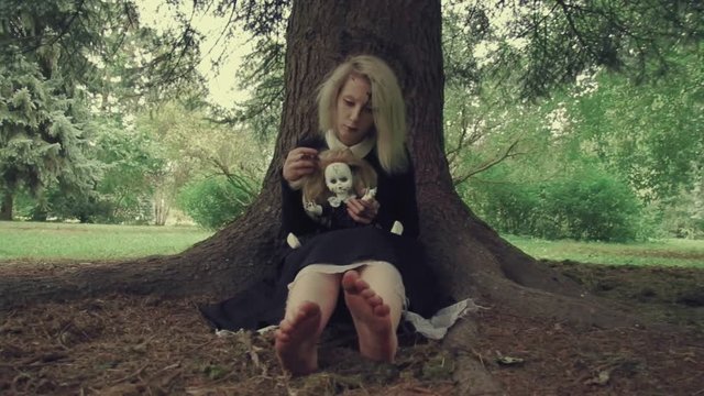 Stylized shot creepy white faced woman with a doll in the grass in the woods