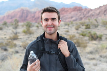 Adventure, travel, tourism, hike and people concept - man holding water bottle and black backpack hiking in the desert rocky mountains 