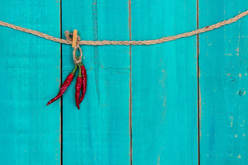 Red hot chili peppers hanging from rope with teal blue wood background