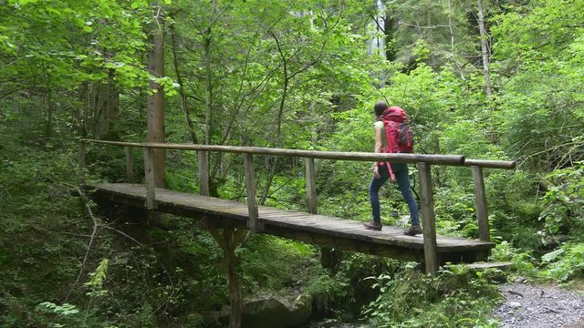 Hiker woman crosses bridge walking to waterfall