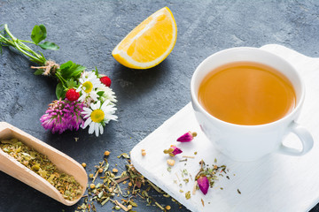 Cup of herbal green tea, lemon wedge, dry herbal tea, rose buds and bouquet of flowers. Concept of antioxidant beverage, healthy lifestyle, dieting, well-being.