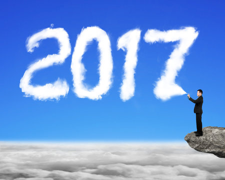 Businessman spraying white 2017 year cloud shape in sky