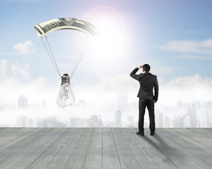 Businessman gazing light bulb with money parachute