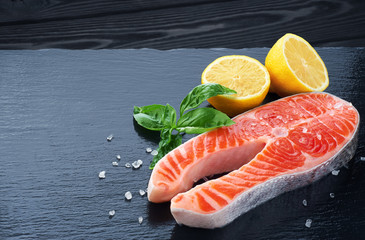Fresh salmon with lemon and basil on a dark background