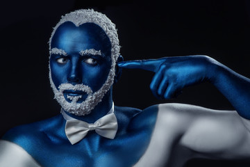 Man painted in blue color with snowy hair and beard gesturing on black background