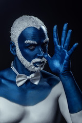 Man painted in blue color with snowy hair and beard gesturing on black background