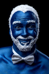 Man painted in blue color with snowy hair and beard grimacing on black background
