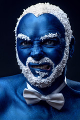 Man painted in blue color with snowy hair and beard grimacing on black background