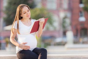 Pregnant woman reading the book on a bench