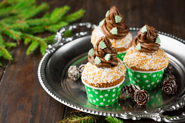 Christmas vanilla Cupcakes with chocolate buttercream icing and holiday decorations on the rustic wooden background